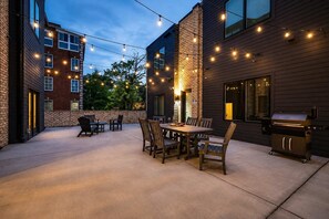 An outdoor patio with a dining table and chairs, a barbecue grill, and string lights.