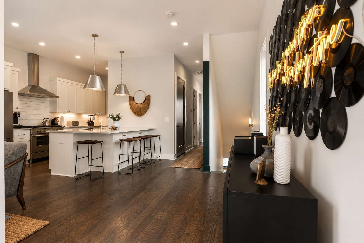 A modern kitchen with a central island, bar stools, pendant lighting, and a wall-mounted record collection.