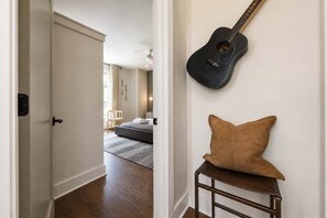 Ein Flur mit einer Gitarre an der Wand, einem braunen Kissen auf einem kleinen Tisch und einem Bett im Hintergrund.