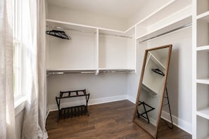 Un dressing accessible sans porte, doté d’étagères ouvertes, d’un grand miroir et d’un porte-vêtements en bois.