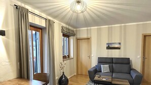 A living room with a sofa, a coffee table, a dining table with chairs, a vase with branches, and a patterned rug. - Apartment Wallberg (Wiefarn Apartments) (Bad Wiessee)