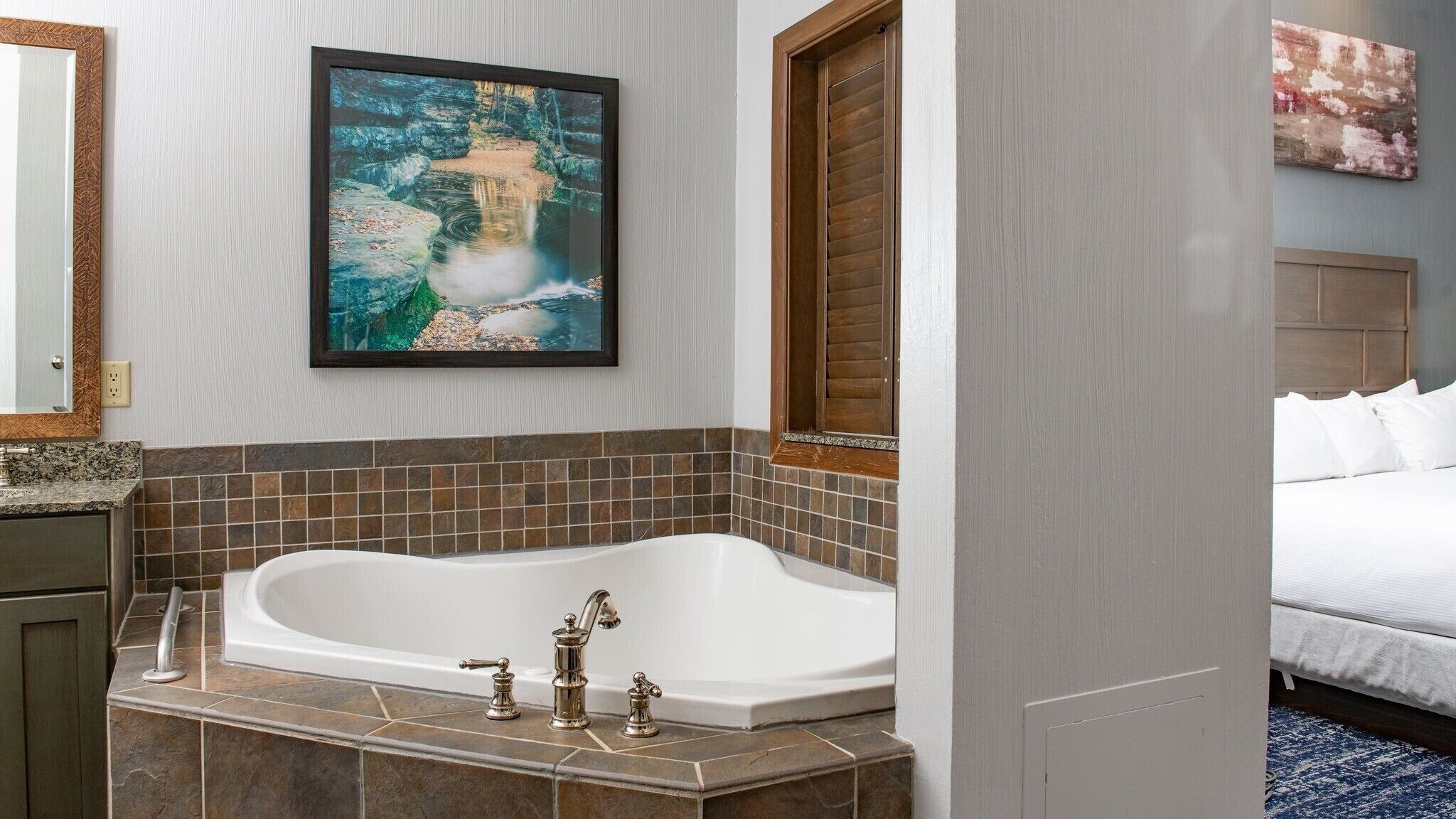 A bathroom with a large bathtub, a framed painting above it, and a wooden door.