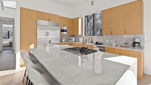 Een moderne keuken met een centraal eiland, roestvrijstalen apparatuur, houten kastjes en een groot raam.