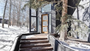 Een besneeuwde pad dat leidt naar een modern huis met een glazen deur en een houten deur.