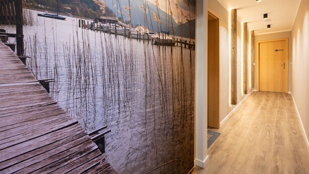 A wooden floor leading to a door, a wooden dock, and a mural of a lake with mountains. - Spacious apartment with sun terrace in the immediate vicinity of the lake (Bad Wiessee)