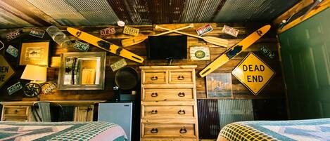A room with two beds, a dresser, a television, and various decorative items including license plates and a 'Dead End' sign.