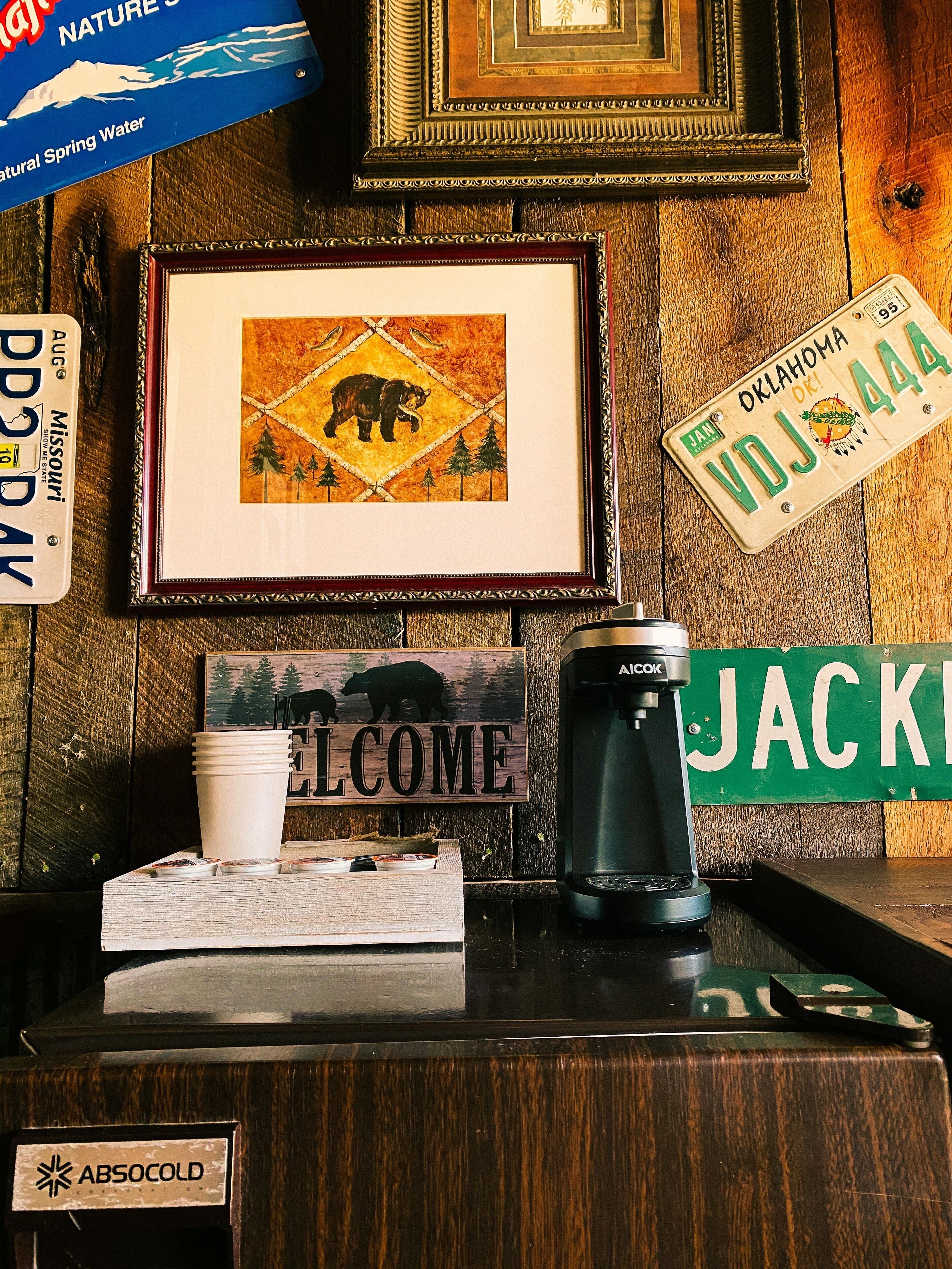 Un comptoir en bois orné d’un tableau représentant un ours, d’une pancarte de bienvenue, d’une machine à café et d’une plaque d’immatriculation.