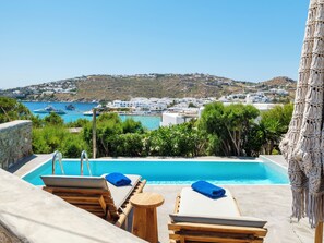 Área da piscina com espreguiçadeiras e vista para uma cidade costeira.