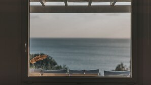 A window with a view of the ocean and a chair with a decorative plant. - MyMykonos Villa II Beach Front  (Mykonos)