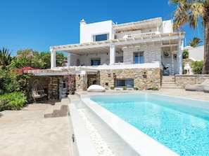 A modern two-story building with a swimming pool, stone walls, and a balcony with white railings. - MyMykonos Villa II Beach Front  (Mykonos)