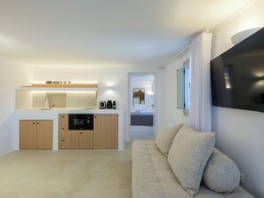A modern kitchen with built-in appliances, a dining area with a table and chairs, and a living room with a sofa and a flat-screen TV. - MyMykonos Villa II Beach Front  (Mykonos)