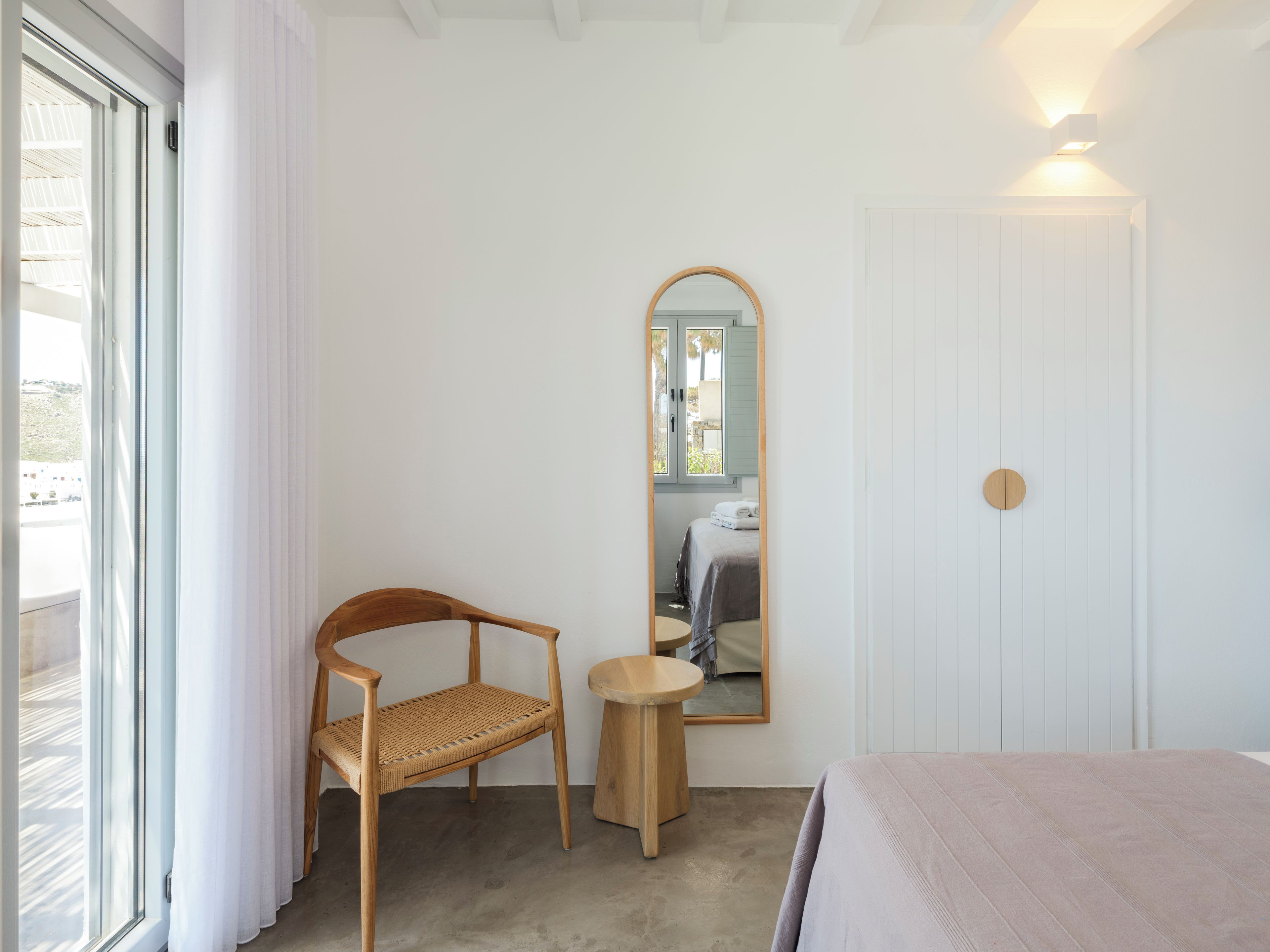 Een slaapkamer met een bed, een stoel, een kleine tafel, een spiegel en een deur.