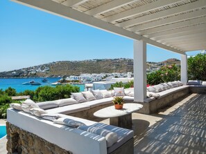 A covered outdoor seating area with a pool, overlooking a coastal town and the sea. - MyMykonos Villa II Beach Front  (Mykonos)