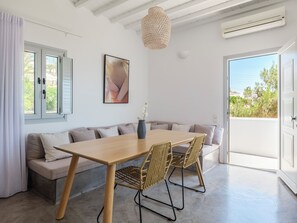 A modern living room with a wooden dining table, wicker chairs, a sofa, and a large window with a view. - MyMykonos Villa II Beach Front  (Mykonos)