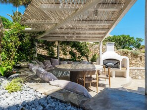 An outdoor seating area with a stone wall, a grill, and a view of the sea. - MyMykonos Villa II Beach Front  (Mykonos)