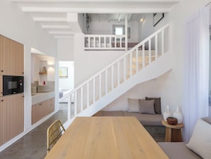 A modern interior with a wooden dining table, a staircase with white railings, and a kitchen area with wooden cabinets. - MyMykonos Villa II Beach Front  (Mykonos)