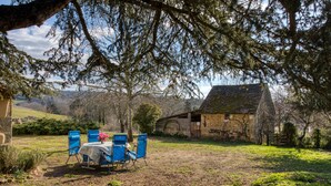 A rustic outdoor seating area with a table and blue chairs, surrounded by trees and a stone building in the background. - La Petite Ferme near DOMME8FP3Q6W9+8R 44.7958121,1.2195112 (Domme)