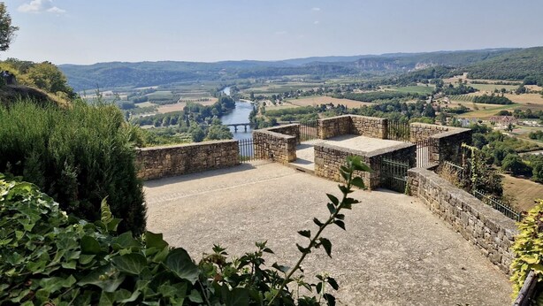A stone structure with a paved area, surrounded by greenery and overlooking a valley with a river and distant hills. - La Petite Ferme near DOMME8FP3Q6W9+8R 44.7958121,1.2195112 (Domme)