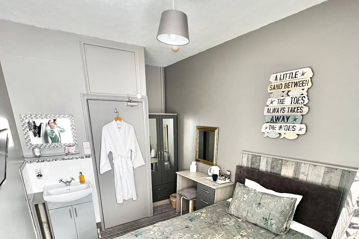 A modern bedroom with a bed, bedside table, mirror, and a wall-mounted sign.