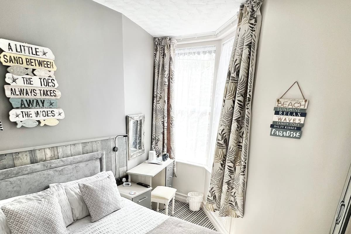 A neatly arranged bedroom with a large bed, a bedside table, a chair, and a window with curtains.