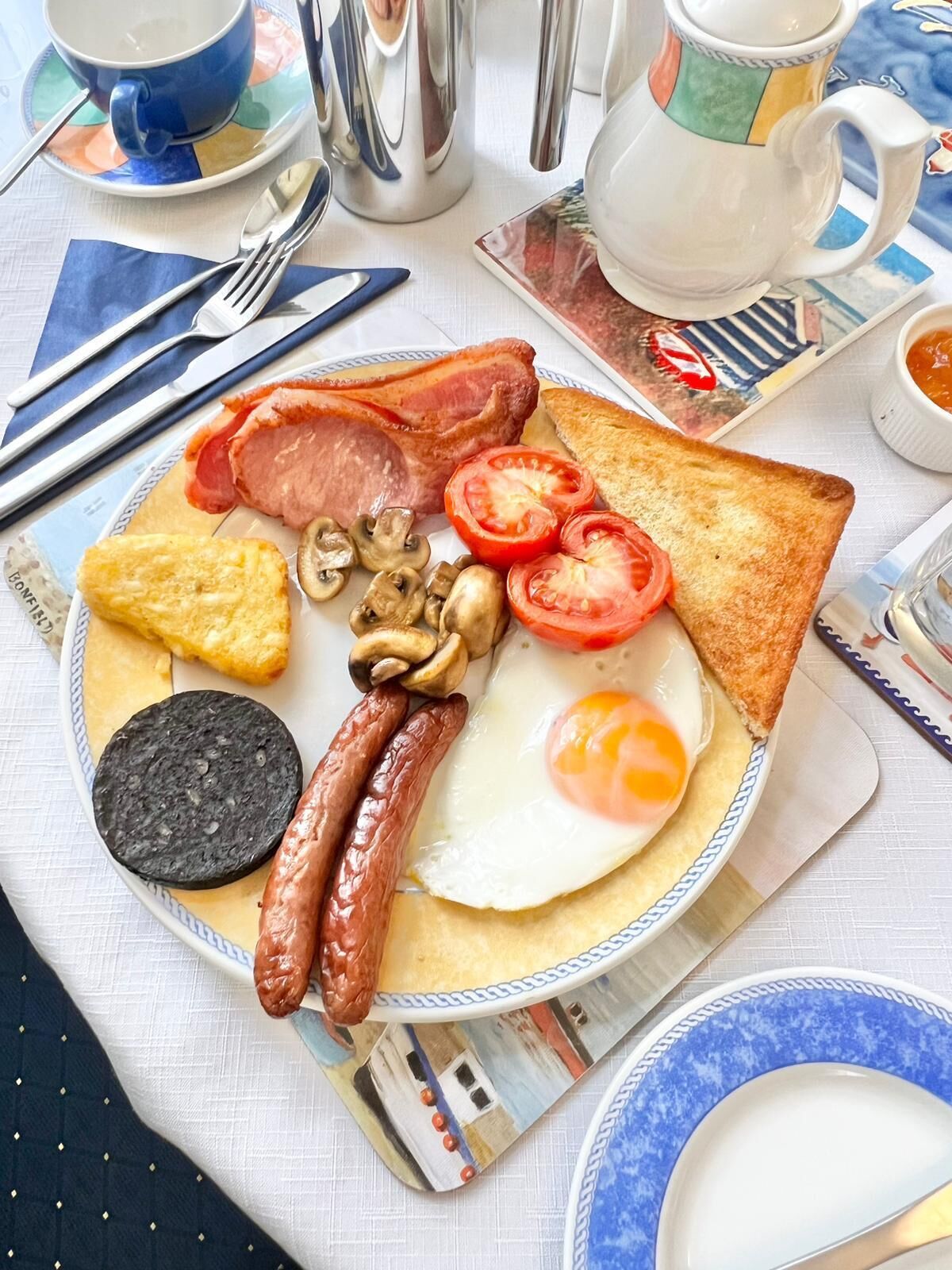 A breakfast plate with bacon, sausages, mushrooms, tomatoes, toast, and a fried egg.
