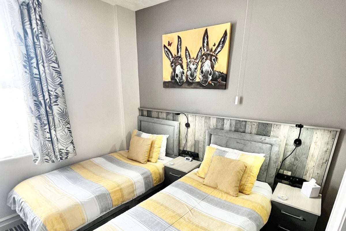 A hotel room with two beds, a wooden headboard, a painting of donkeys, and a striped rug.