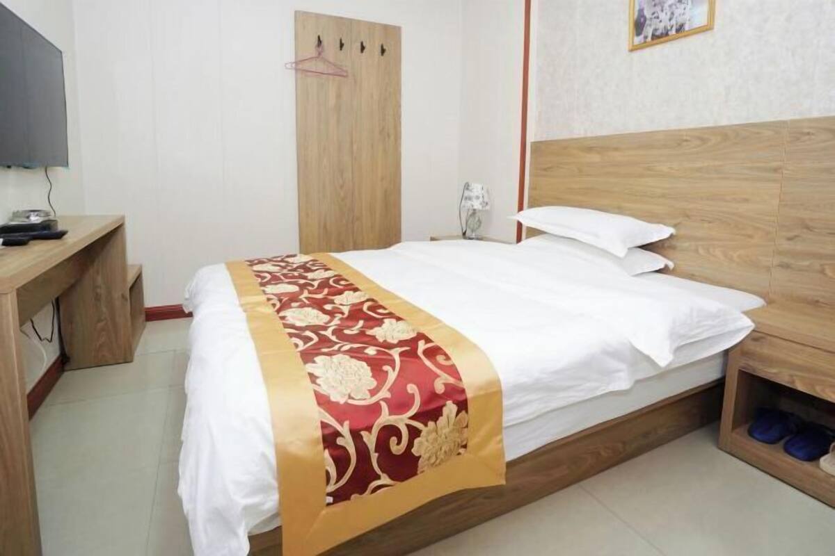 Una habitación de hotel con cama, escritorio, televisor, armario y zapatero.