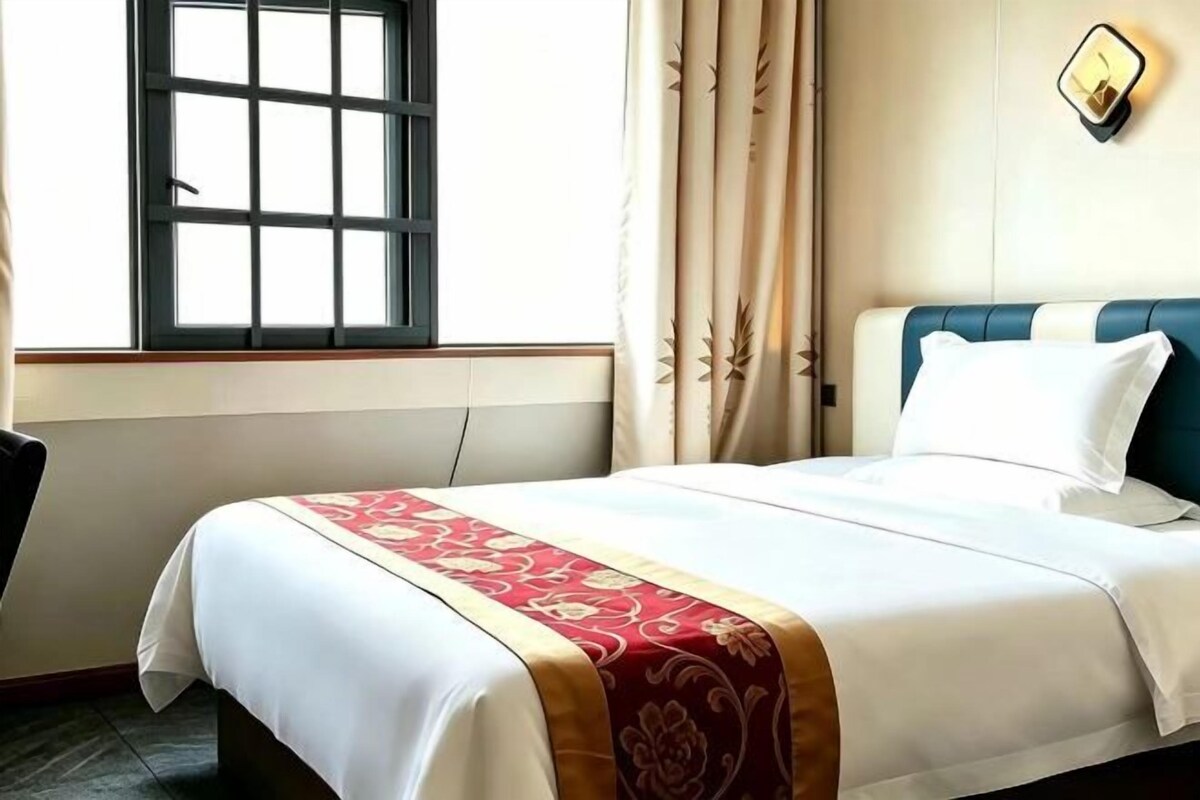 Une chambre d’hôtel avec un lit, des rideaux, une fenêtre et un luminaire fixé au mur.