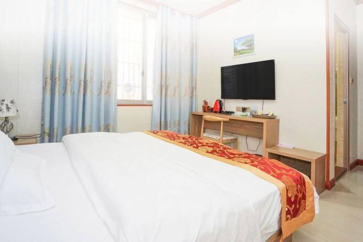 Una habitación de hotel con cama, escritorio, televisión y ventana con cortinas.