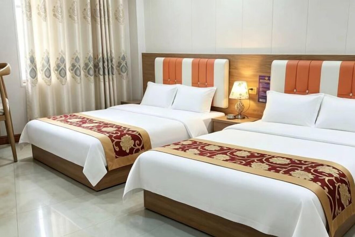 A hotel room with two beds, a nightstand with a lamp, and a wooden headboard.