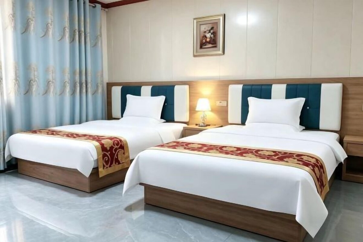 A hotel room with two beds, a nightstand with a lamp, and a wall-mounted picture.