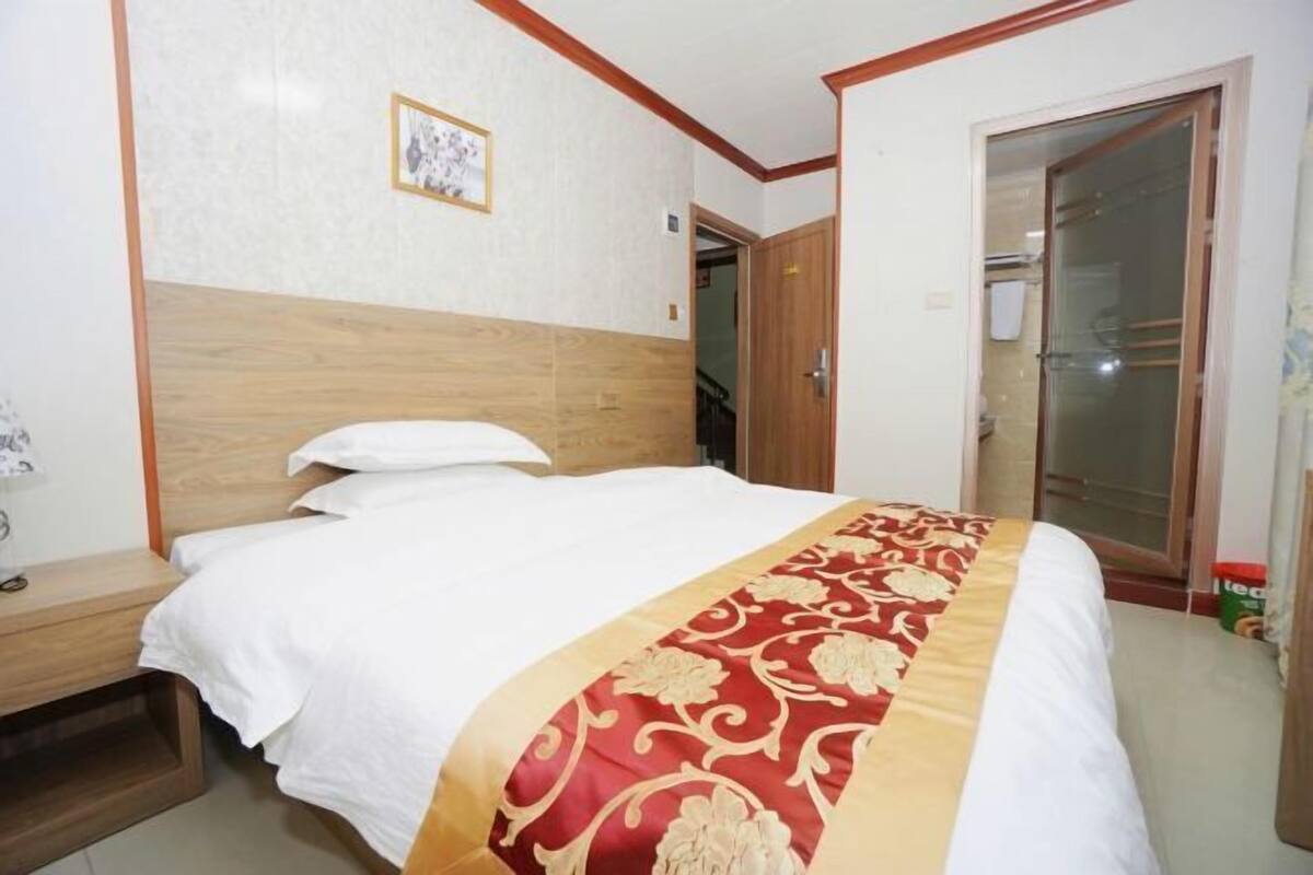 Una cama bien hecha con una colcha roja y dorada, un cabecero de madera y una mesita de noche con una lámpara.