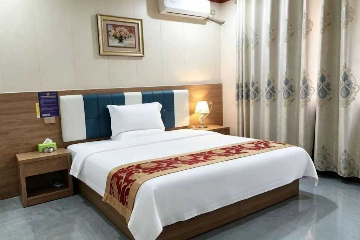 A hotel room with a bed, bedside table, lamp, and curtains.