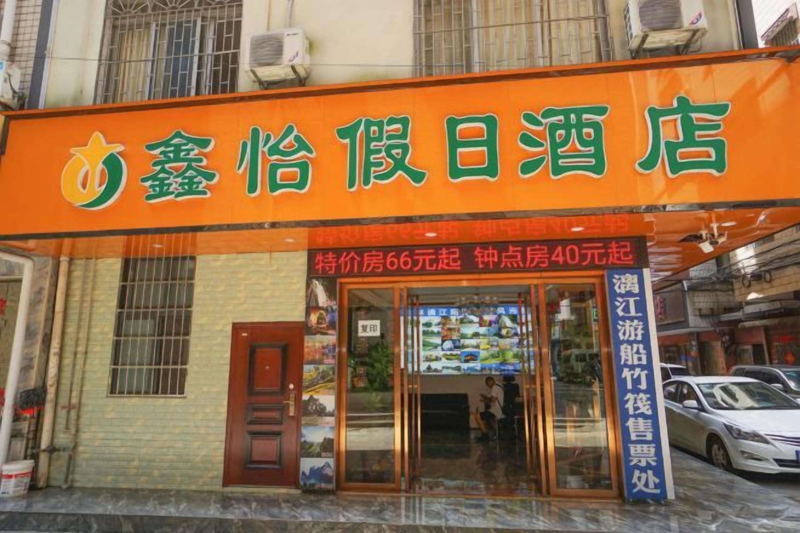 A hotel with an orange signboard, a visible entrance, and a car parked outside.