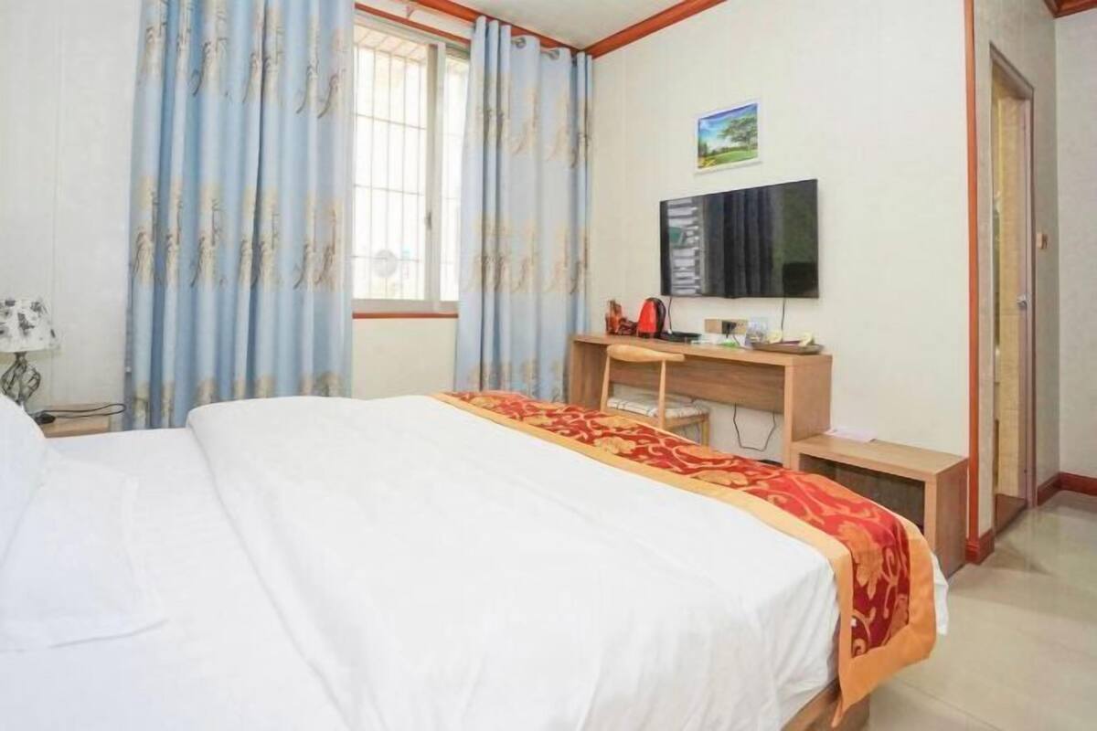 Una habitación de hotel con cama, escritorio, televisor y cortinas.
