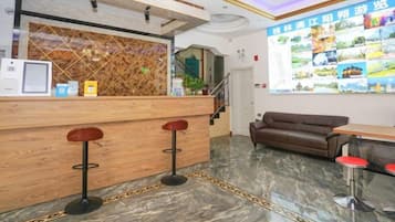 A reception area with a wooden counter, two bar stools, a brown sofa, and a wall with a map.