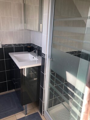 Ein Badezimmer mit einem weißen Waschbecken, schwarz-weißen Fliesen an den Wänden und einer Duschkabine aus Glas.