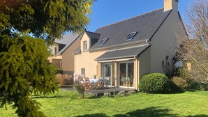 Ein Haus mit großem Rasen, einer Terrasse mit Gartenmöbeln und einem überdachten Bereich mit Tisch und Stühlen.