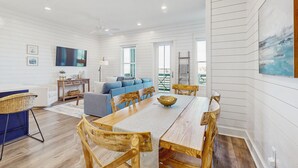 A spacious living area with a wooden dining table, blue sofa, and a television mounted on the wall. - Spacious & modern home with gleaming kitchen, pool access & balcony (Port Aransas)