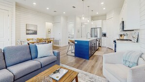 A modern living room with a grey sofa, a white sofa, and a wooden coffee table. There is a kitchen area with white cabinets and a blue island. - Spacious & modern home with gleaming kitchen, pool access & balcony (Port Aransas)