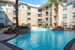 A swimming pool with a palm tree, surrounded by a multi-story building with balconies.