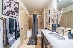 A modern bathroom with a bathtub, toilet, and sink. There are towels hanging on the wall, a rug on the floor, and a mirror with a vase of flowers.