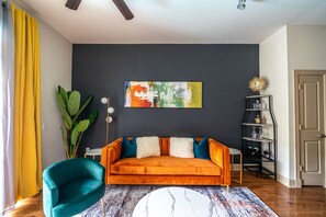 Un salon comprenant un canapé, un fauteuil turquoise, une table basse, une lampe sur pied et une bibliothèque.