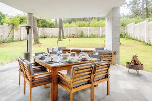 An outdoor patio with a wooden table and chairs, surrounded by a concrete floor and a stone wall.