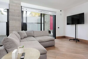 A modern living room with a sectional sofa, a flat-screen TV mounted on the wall, and a sliding glass door leading to an outdoor area.