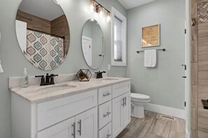Een badkamer met een dubbele wastafel, toilet, douche en een handdoekrek met een handdoek.