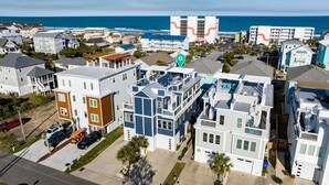 A coastal residential area with modern multi-story buildings, a parking lot, and a view of the ocean. - SeaRenity with rooftop and ocean views (Carolina Beach)