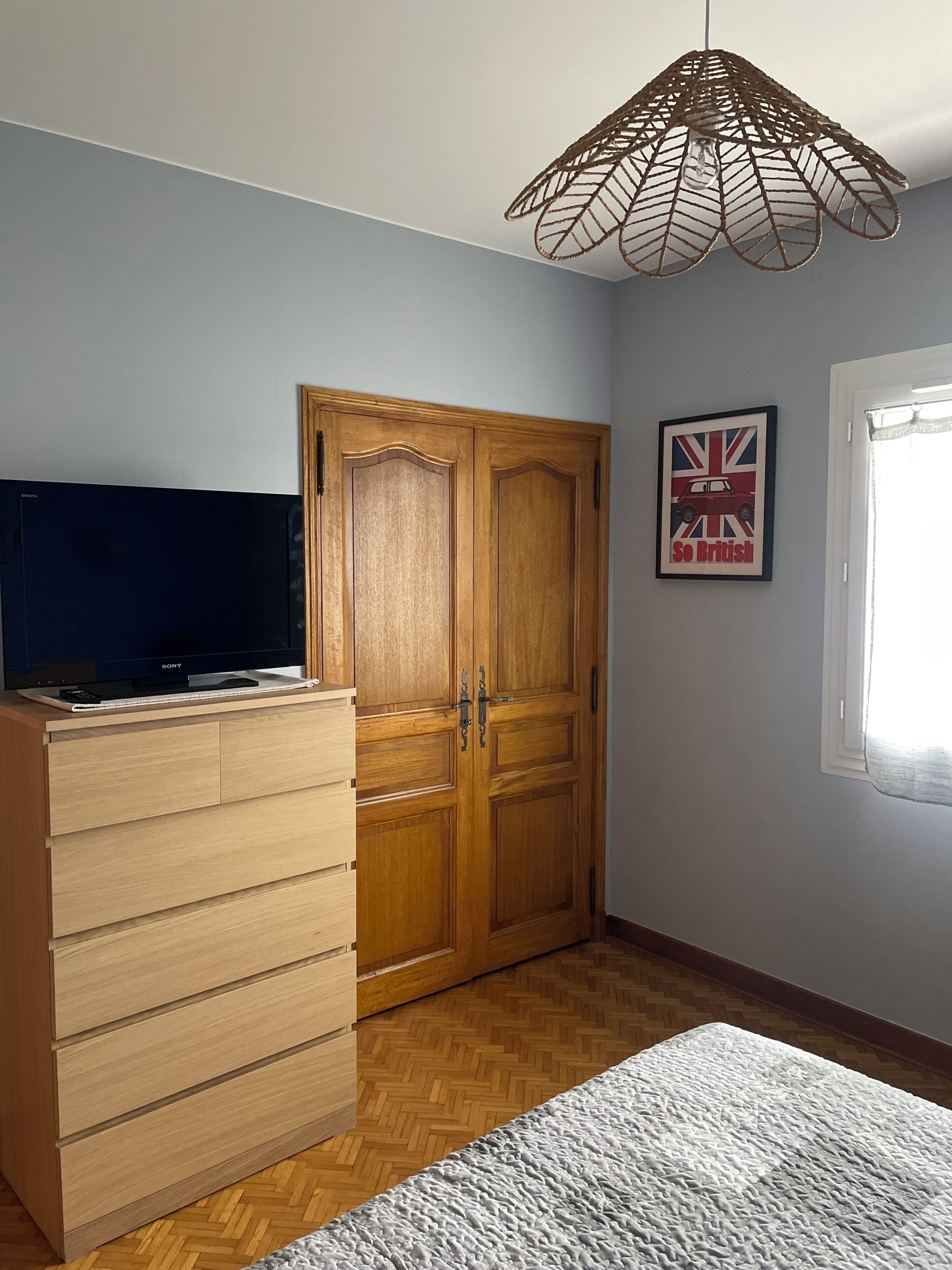 Una habitación con un armario, un televisor sobre un mueble de madera, un cuadro en la pared y una ventana.