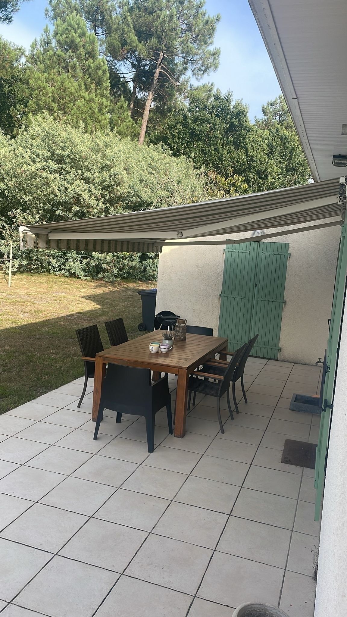 En terrasse med et træbord og stole, en grøn dør og et flisegulv.