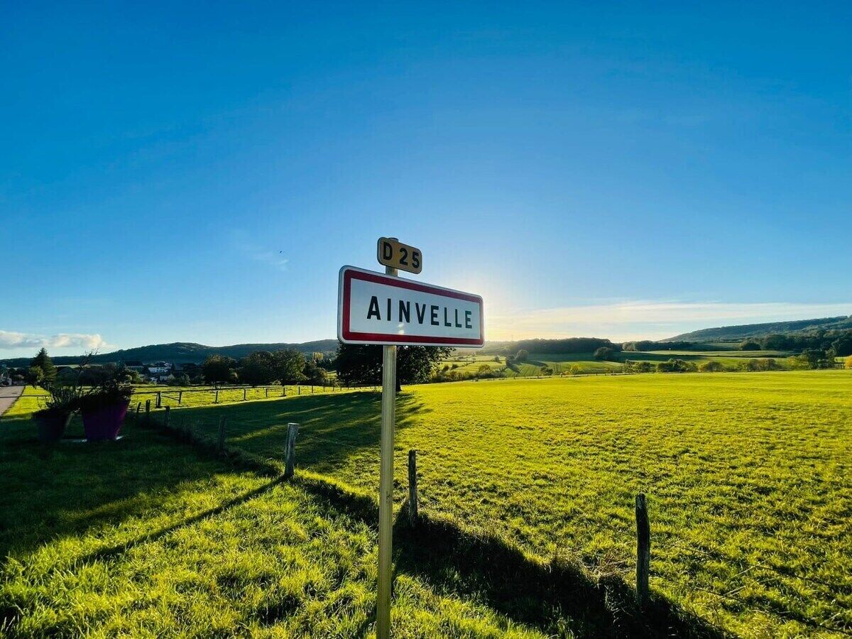A rural landscape with a sign reading "AINVELLE" and a road number "D 25".